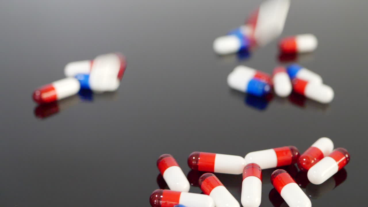 Close up on drug pills and antidepressant medicine capsules in slow motion on a black isolated background
