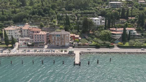 Vista-Aérea-Del-Paseo-Del-Lago-En-El-Lago-De-Garda-Con-Casas-Al-Fondo-Y-Autos-En-La-Carretera-En-Un-Día-Soleado