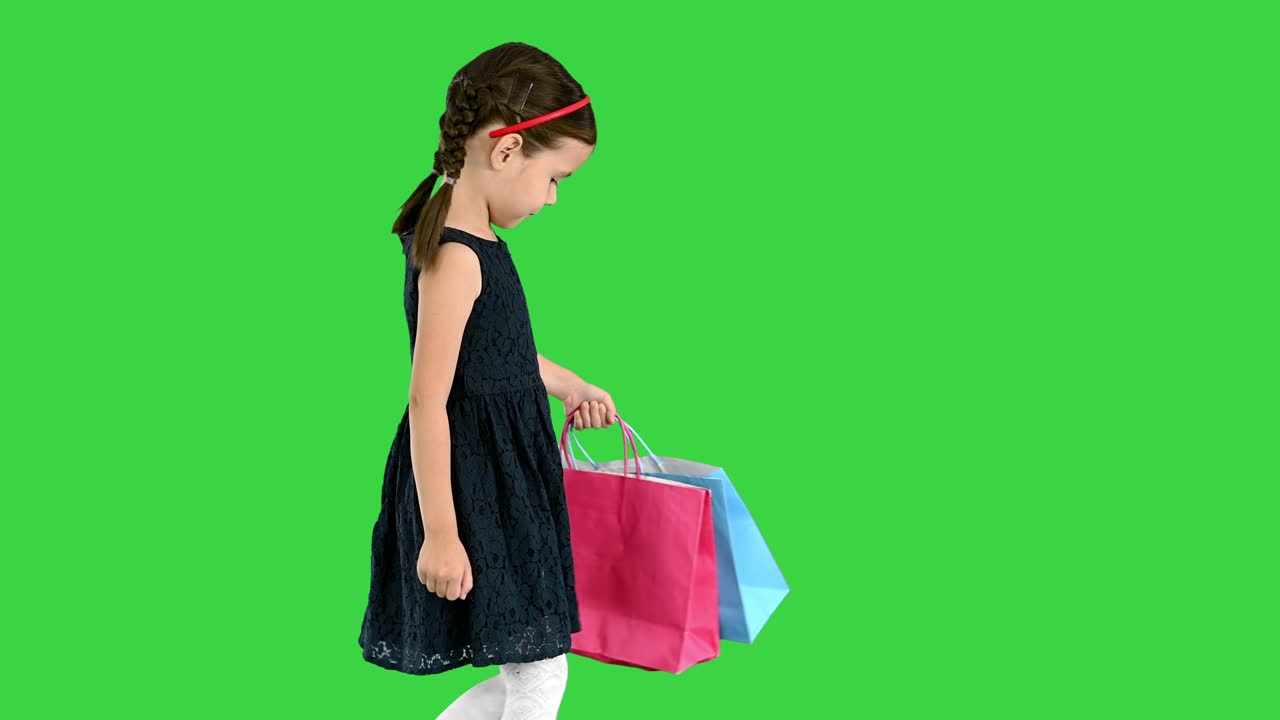 Beautiful little girl in black dress walking with shopping bags on a Green Screen, Chroma Key