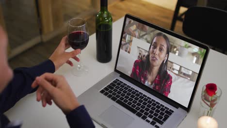 Mixed-race-man-sitting-at-table-using-laptop-making-video-call-with-female-friend