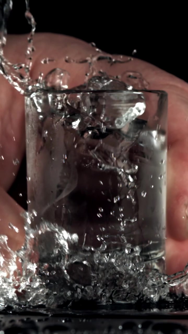 Acqua che si versa e schizza in un bicchiere con ghiaccio al rallentatore
