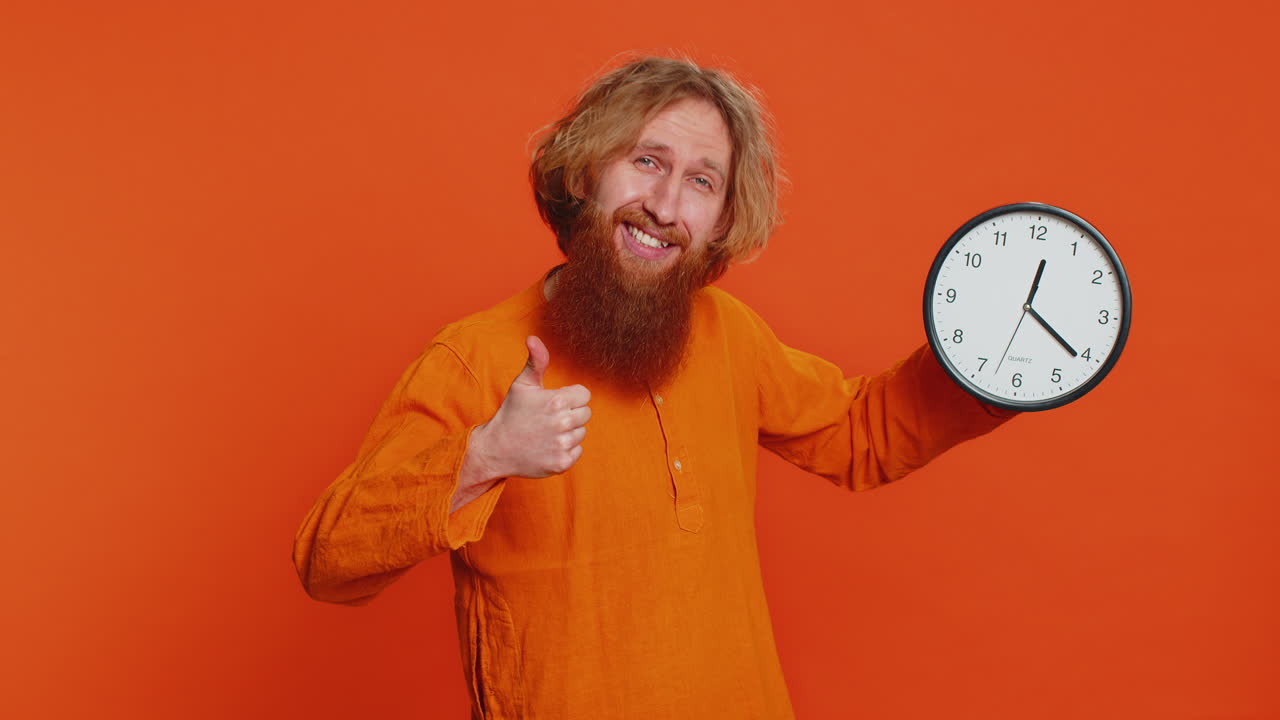 возбужденный белый мужчина показывает время час на стене офисные часы хорошо большой палец вверх одобрить поторопитесь крайний срок