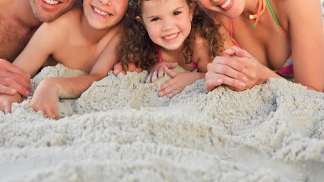 Portrait-of-smiling-caucasian-family-on-holiday-lying-on-sand-by-sea