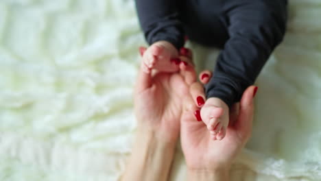 mom holding little tender baby feet and caressing them. loving mum's touches of tiny toes of her child. close up.
