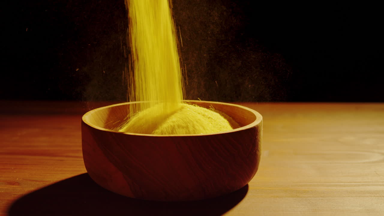 Yellow Powder Pouring into a Wooden Bowl