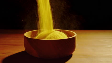 yellow powder pouring into a wooden bowl
