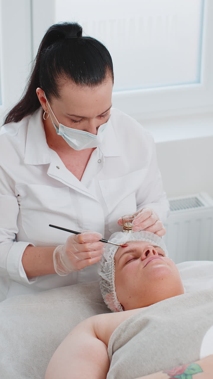 Kosmetolog påfører fugtgivende medicinsk kemisk peeling creme maske på ung voksen kvindes ansigt