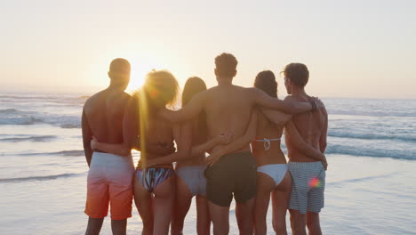 rear view of friends watching sunset on summer beach vacation