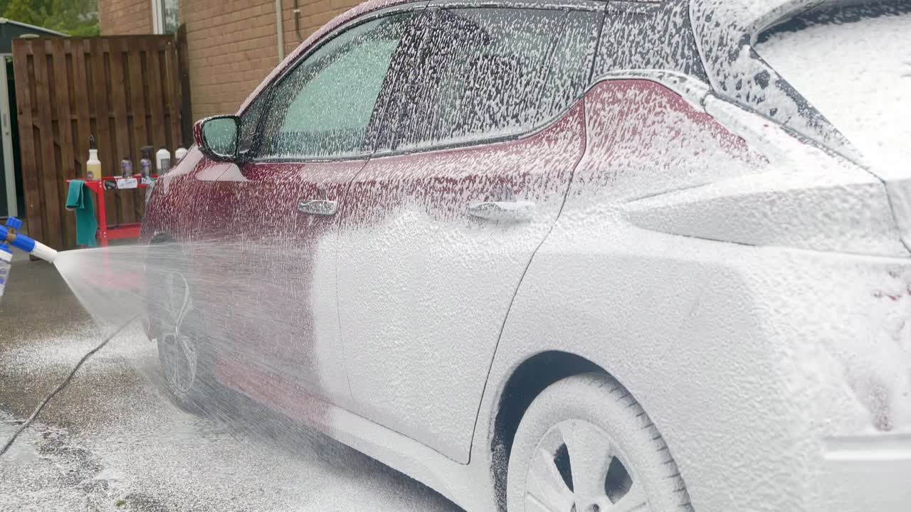 Applying a thick blanket of snow foam shampoo to a dark red car