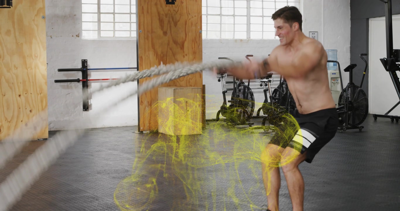 Man gripping battle ropes, initiating waves in gym, rising, lowering for power, yellow glow on legs