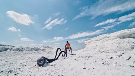 shirtless man during working out with battle ropes in nature. young muscular man training with ropes on the mountain against the blue sky. high intensive workout.