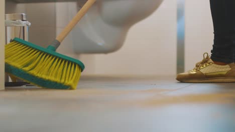 female worker cleaning the bathroom floor with a bathroom sweeping broom - close up