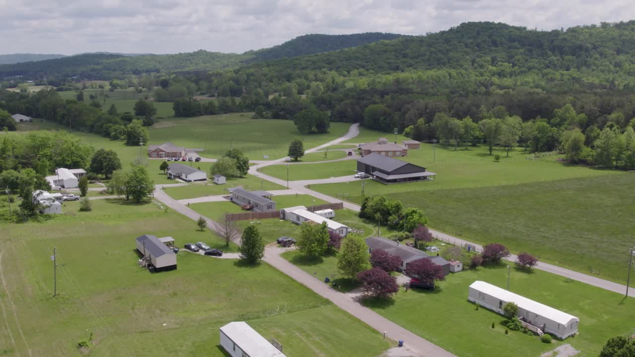 Aerial view of a quiet neighborhood nestled beneath a large green hill in Kentucky. Ideal for real estate, local living, or regional landscape footage.