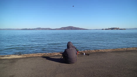 person fishing and sitting on seaside with alcatraz island in the background in san francisco bay