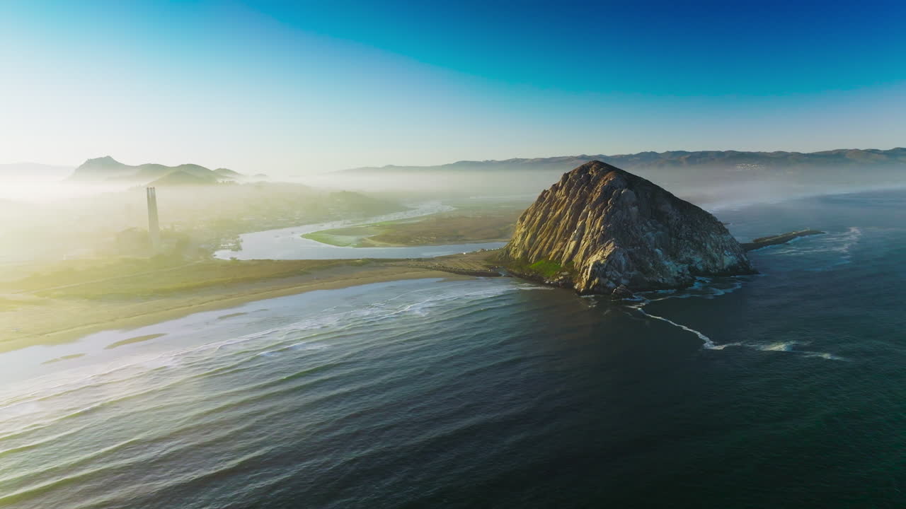 Magical sight of Morro Bay covered with thick fog. Triangle rock at the shore of Central coast of California, USA . Azure sky at backdrop.