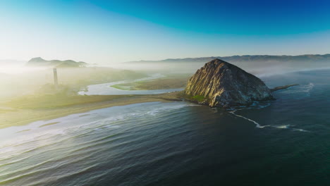 magical sight of morro bay covered with thick fog. triangle rock at the shore of central coast of california, usa . azure sky at backdrop.
