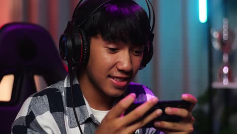 close up of asian teen boy gamer smiling to camera and showing thumb up while playing video game on smartphone