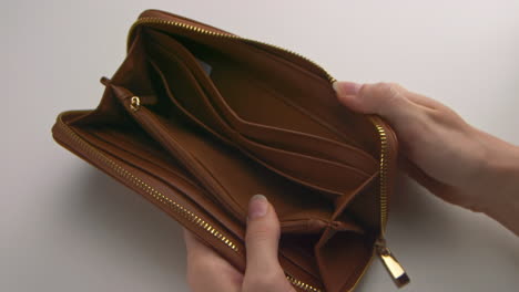 a caucasian woman's hands opening and showing an empty brown wallet