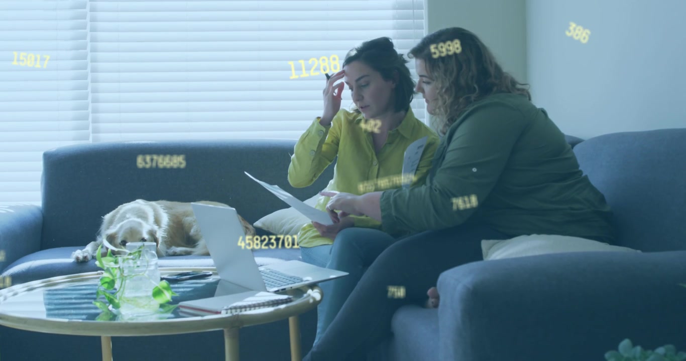Due donne che sistemano documenti, controllano il laptop e confrontano dati finanziari con sovrapposizione numerica