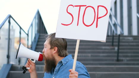 nahaufnahme eines bärtigen kaukasiers, der über einen lautsprecher spricht und ein stoppschild auf der straße hält