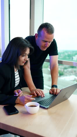 caucasian man stands near his female colleague. man looks at the laptop screen tensely using touchpad. vertical video.