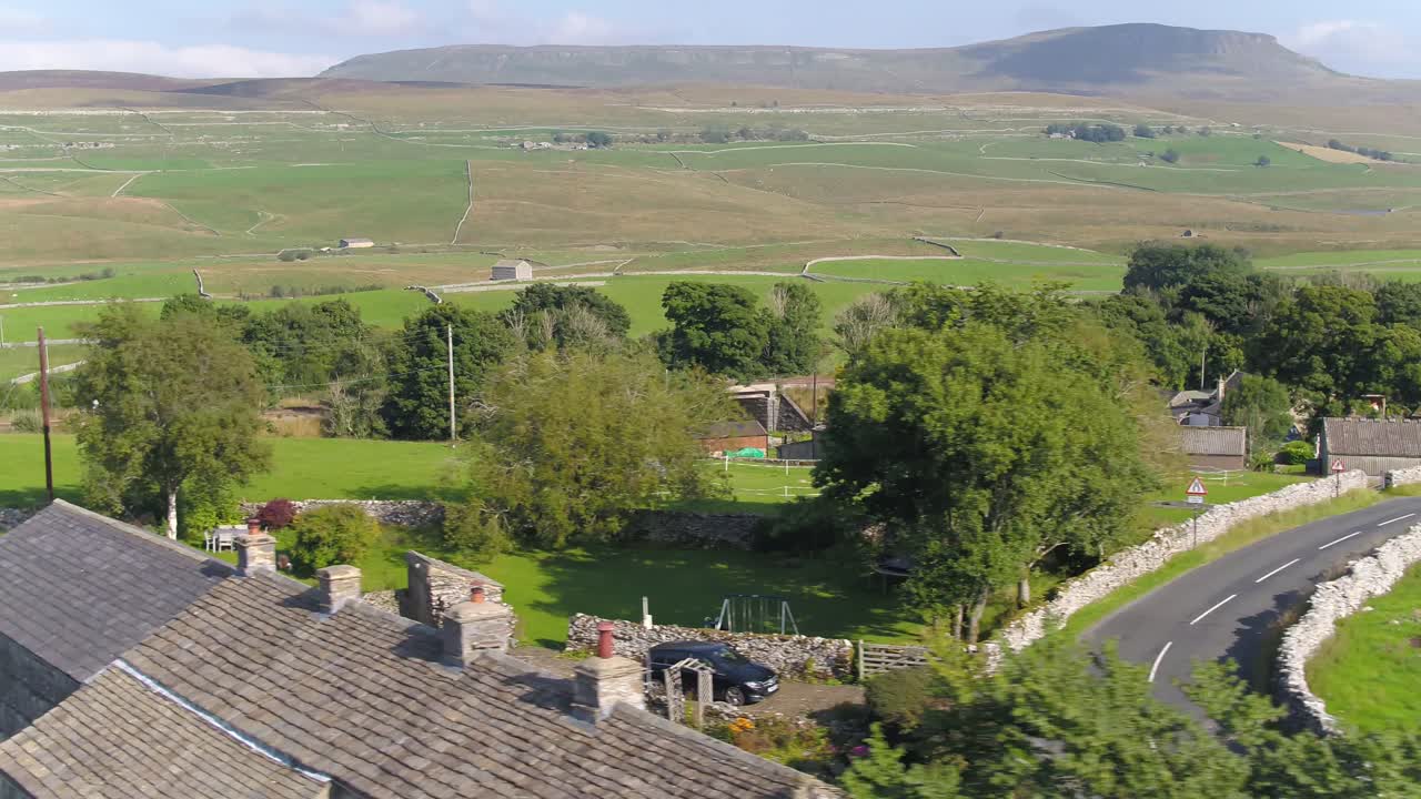 imágenes de drones volando bajo sobre una carretera de campo de pared de piedra seca y detrás de un techo y árboles que muestran el campo de yorkshire y los campos con la montaña de penn y ghent en la distancia