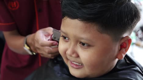 niño asiático feliz peinado en la barbería