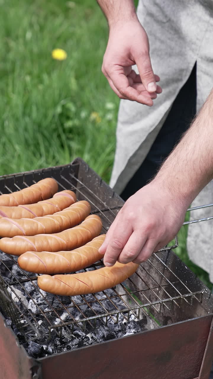 Man hands grilling tasty sausages on barbeque. Delicious grilled meal on fire. Vertical video