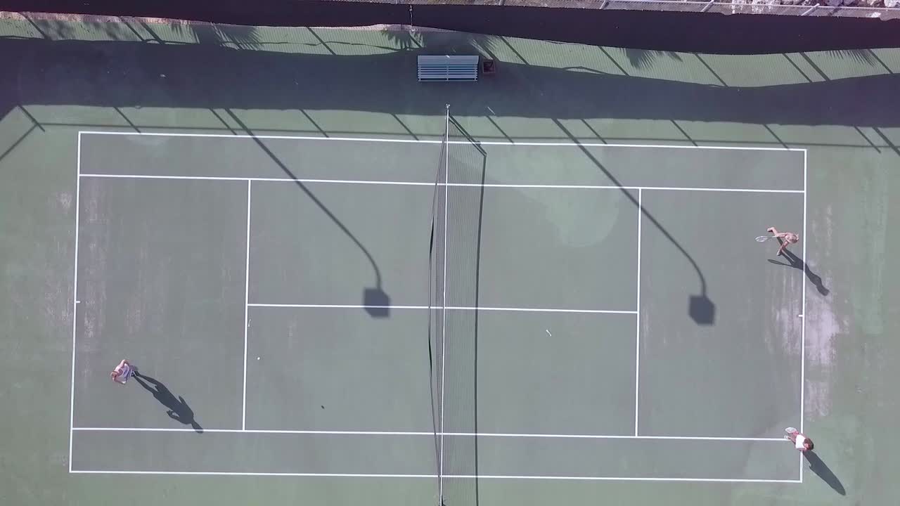 테니스 코트에서 테니스 경기를 하는 사람들 위에 높은 각도의 드론 공중