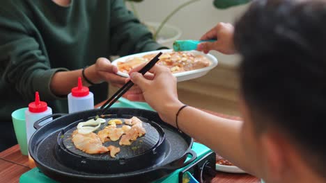 friends cook together on tabletop grill, sharing food and casual meal. focus on hands and collaborative dining experience