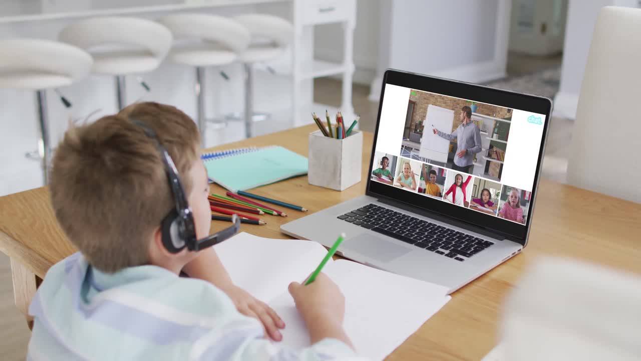 Schoolboy using laptop for online lesson at home, with diverse teacher and class on screen