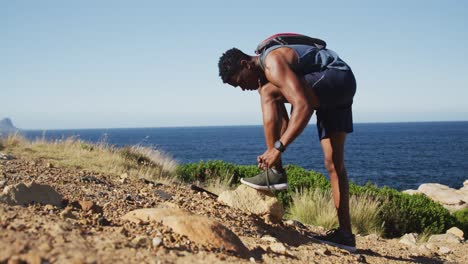 African-american-man-exercising-outdoors-tying-his-shoe-in-countryside-on-a-coast