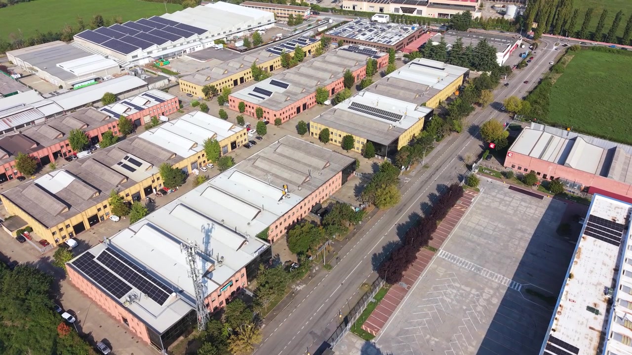 Aerial View of an Italian industrial district showing warehouse architecture, solar-equipped rooftops, parking spaces and vehicles.