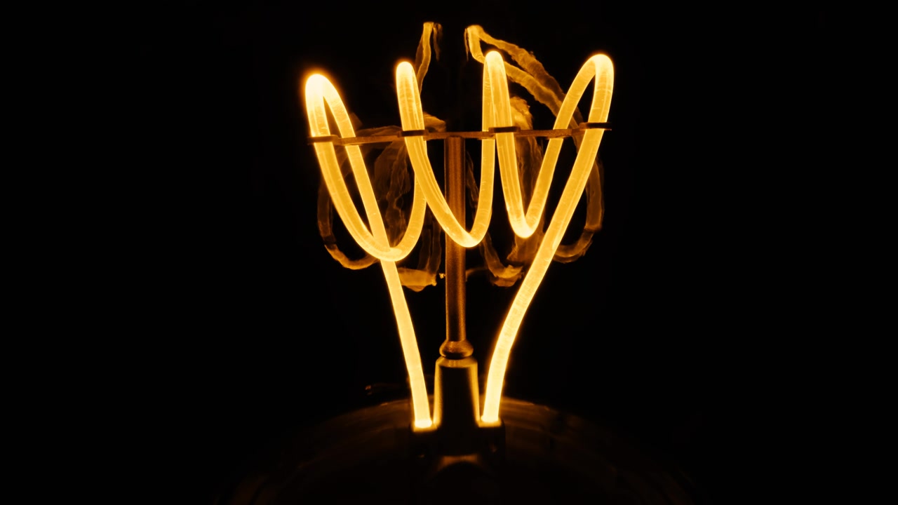 Lampada a incandescenza al tungsteno tremolante con una spirale arancione macro. Lampada a spirale incandescente in primo piano su sfondo nero. Video raw 4k in loop.