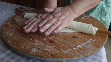 las manos de la abuela amasan la masa para la tarta con un palo de madera, preservando el patrimonio culinario tradicional