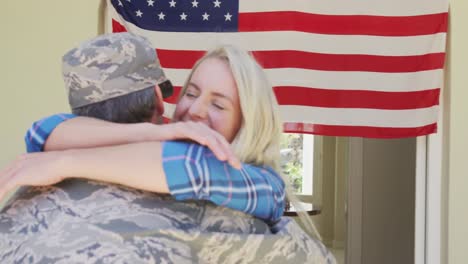 Caucasian-male-soldier-embracing-his-smiling-wife-over-american-flag