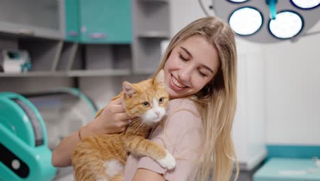 Portrait-of-a-happy-blonde-girl-holding-an-orange-white-cat-in-her-arms-during-an-appointment-at-a-veterinary-clinic-examining-pets