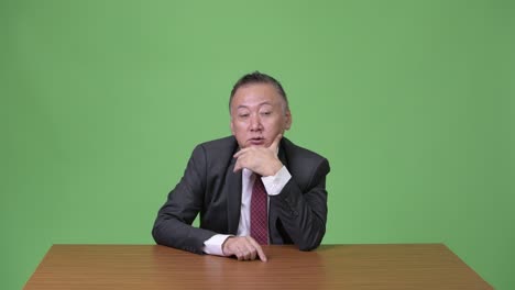 mature japanese businessman looking bored against green background