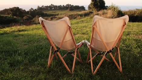 sillas de madera frente a un prado verde exuberante con vistas al océano lejano