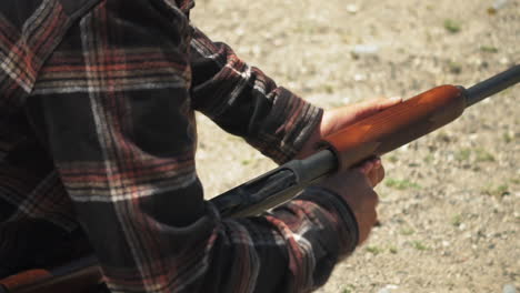 man with checkered shirt loading pump action shotgun ammo from underneath