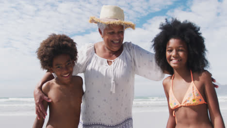 Porträt-Einer-älteren-Frau-Mit-Gemischter-Abstammung-Und-Lächelnden-Enkelkindern-Am-Strand