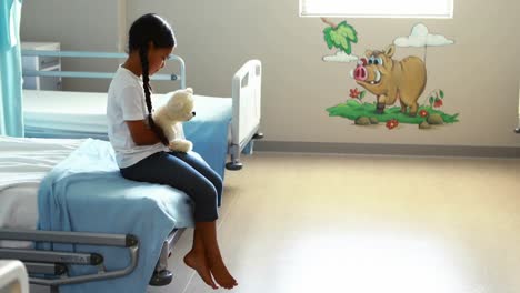 sick girl sitting on bed with teddy bear