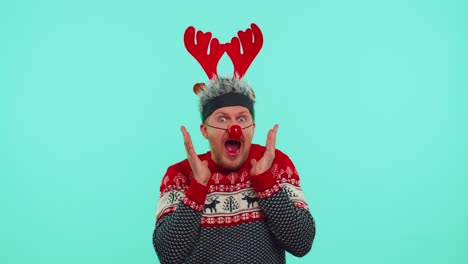 Man-wears-red-New-Year-sweater-deer-raising-hands-in-surprise-shocked-by-sudden-victory,-wow-emotion