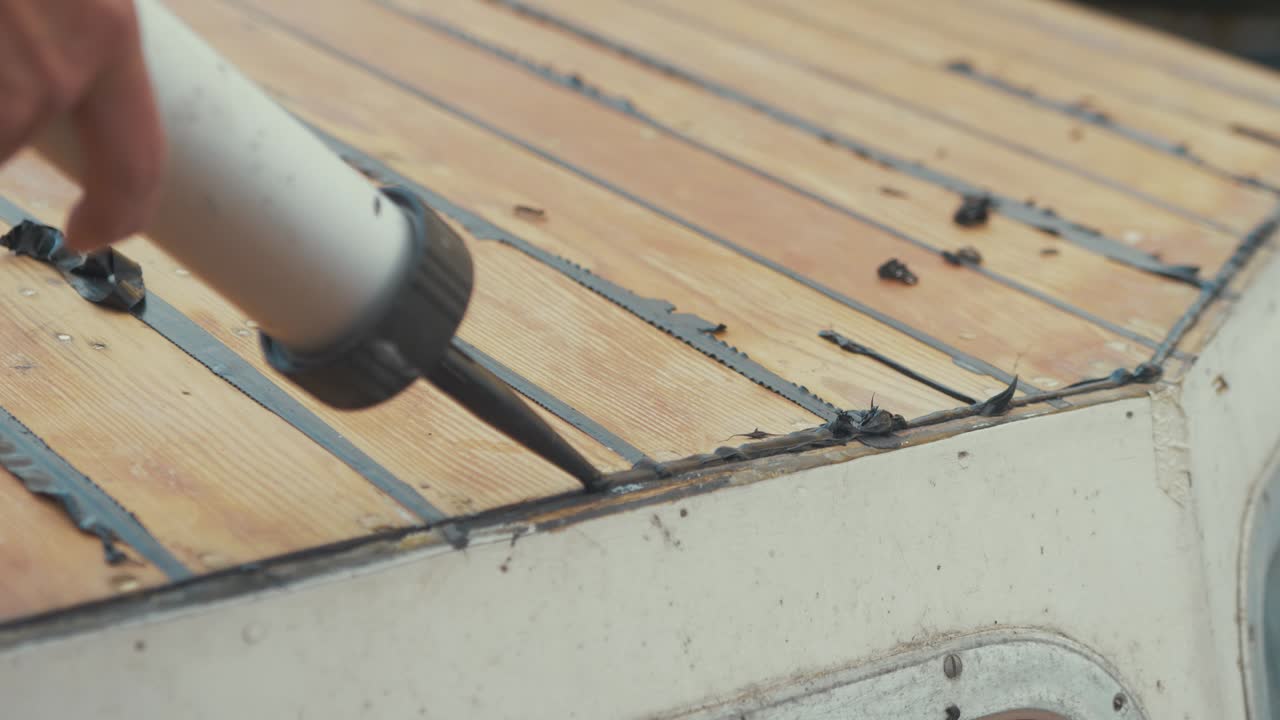 joven carpintero sellando el borde del techo de madera contrachapada del techo de la cabina del barco con sika flex