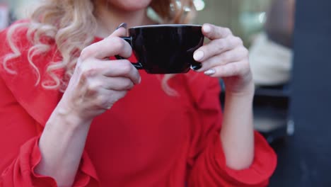 black cup of coffee in female hands on a red background. outdoor shooting on the street