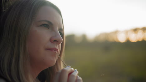 close-up of business woman lost in thought, gently rotating a strand of hay in fingers, warm golden sunlight highlights her contemplative expression, with a blurred countryside background