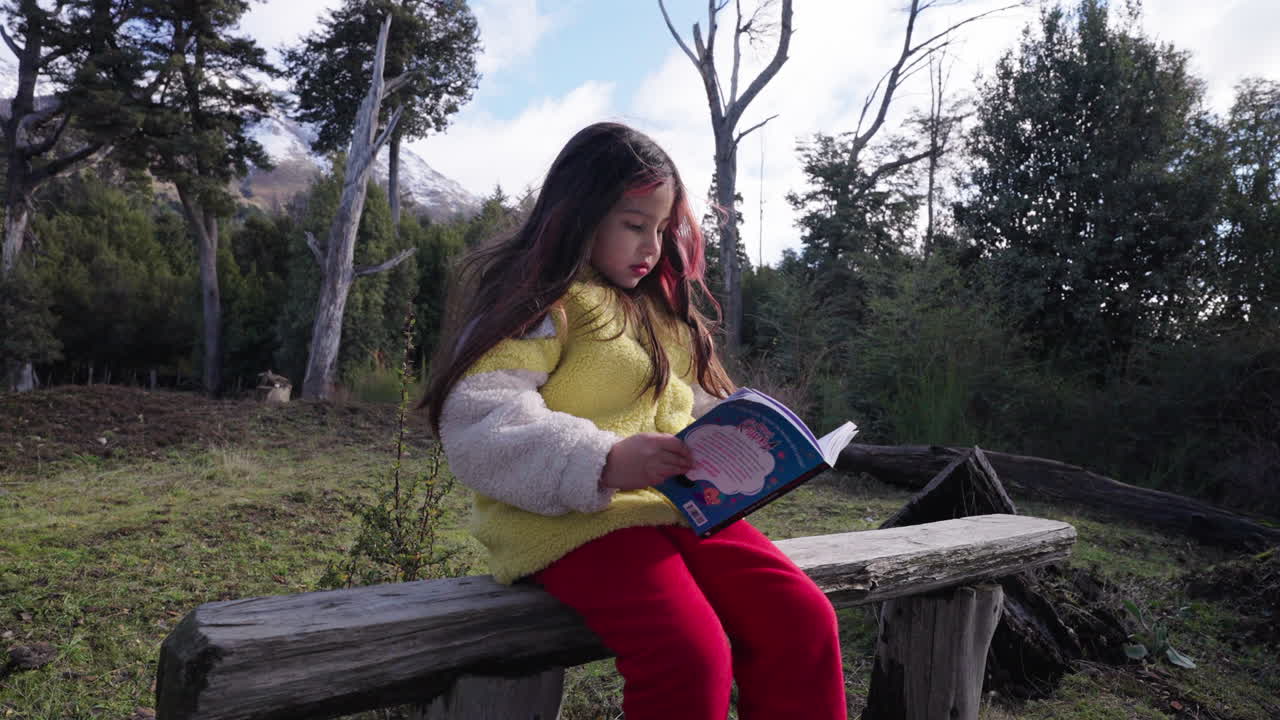 A girl sits quietly on a bench, absorbed in reading a book amid peaceful nature