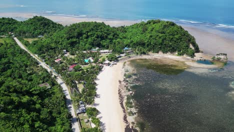 aerial forward drone shot of tropical white sand beach resort with lush hills and shallow reef during low tide