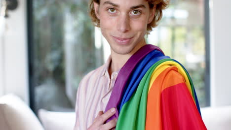 Portrait-of-happy-caucasian-man-holding-rainbow-lgbt-flag-at-home,-slow-motion