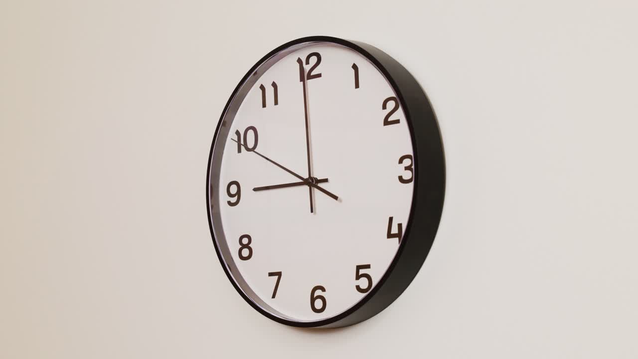 A detailed close-up of a wall clock with a black frame and white face, displaying the time at 9:00.